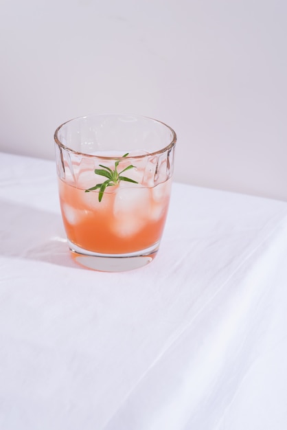 Rosa Cocktail mit Rosmarin und Eis im Glas auf einer weißen Tischdecke auf dem Tisch