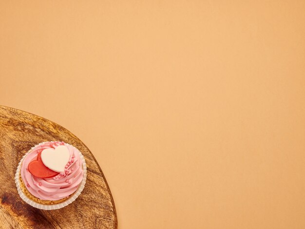 Rosa Cupcakes Kuchen mit Herzen auf einem Küchenholzbrett auf einem beige braunen Hintergrund