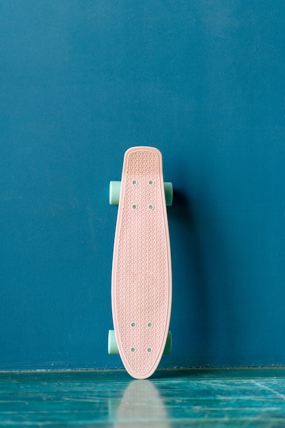 Foto rosa de plástico skate em pé perto de uma parede azul. cruzador fêmea plástico contra o fundo azul da parede