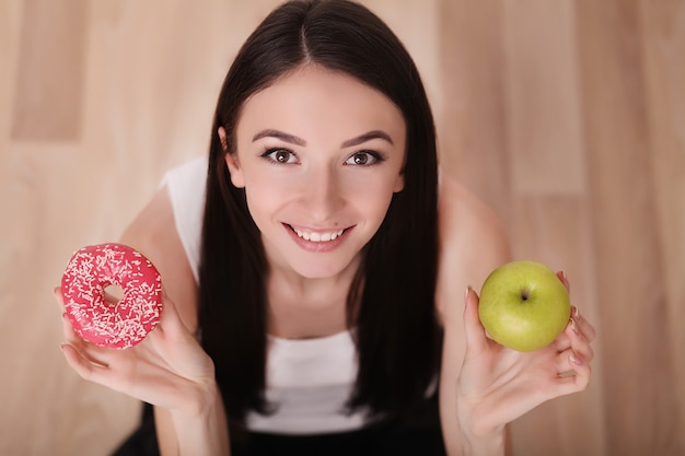 Rosa Donut des dünnen Frauengriffs in der Hand und grüner Apfel