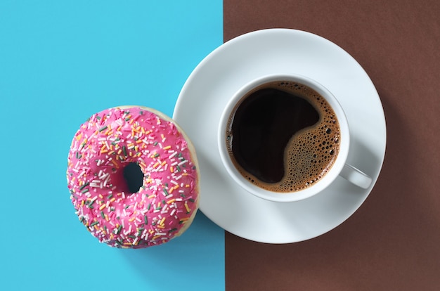 Rosa Donut mit Streuseln und Tasse Kaffee auf zweifarbiger Hintergrundansicht von oben