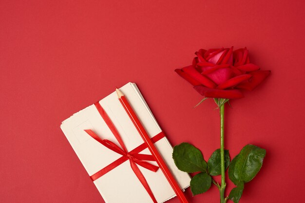 Rosa floreciente roja, una pila de tarjetas de papel vintage y lápiz de madera rojo