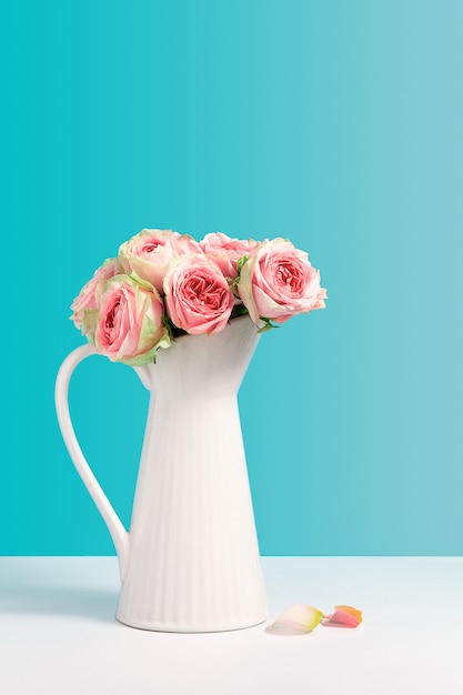 Foto rosa fresca no suporte cerâmico branco do vaso no fundo azul. composição de minimalismo com flores, vaso com espaço de cópia de texto. conceito de loja de flores. cartão de felicitações