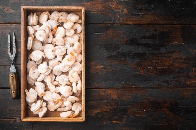 Rosa gefrorene Garnelen mit Eis. Ungekochte geschälte Meeresfrüchte in Holzkiste auf altem dunklem Holztisch, Draufsicht flach gelegt