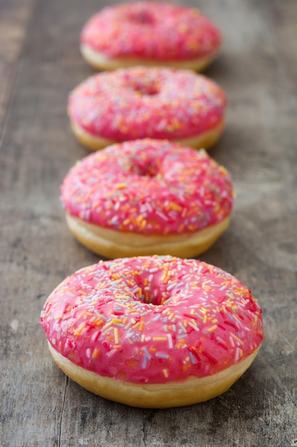 Rosa gefrosteter Donut mit bunten Streuseln auf Holztisch