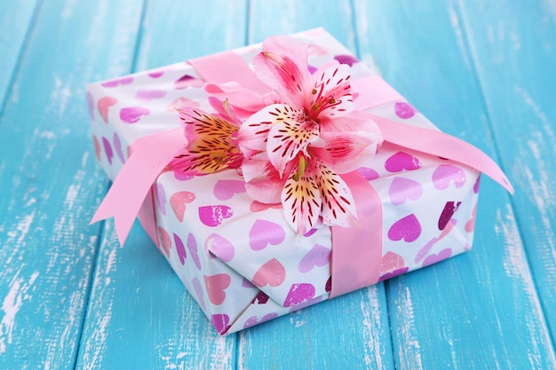 Foto rosa geschenk mit schleife und blume auf holztisch nahaufnahme