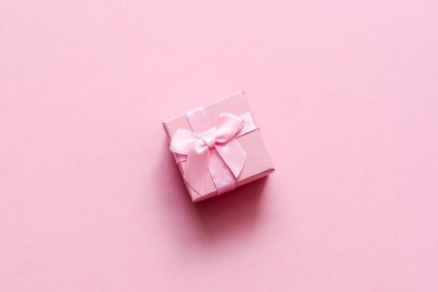 Foto rosa geschenkbox mit bogen auf rosa pastellhintergrund. festliche kulisse. ansicht von oben platz kopieren.