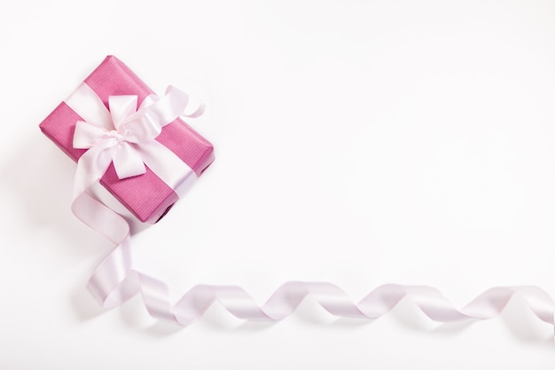 Foto rosa geschenkbox, weiße schleife, langes gebogenes band und leerer raum für text auf weißem hintergrund.