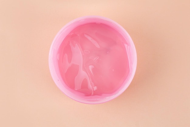Rosa Glas mit transparentem Kosmetikgel auf beigem Hintergrund, Nahaufnahme Kosmetologie- und Schönheitskonzept