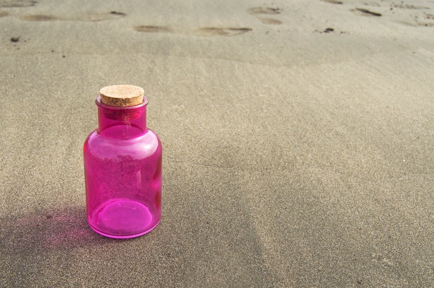 Rosa Glasflasche mit Korkenstopper auf dem Strandsand