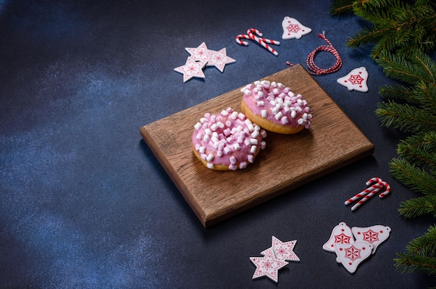 Rosa glasierter Donut und Marshmallow mit Weihnachtsschmuck auf einem Holzschneidebrett