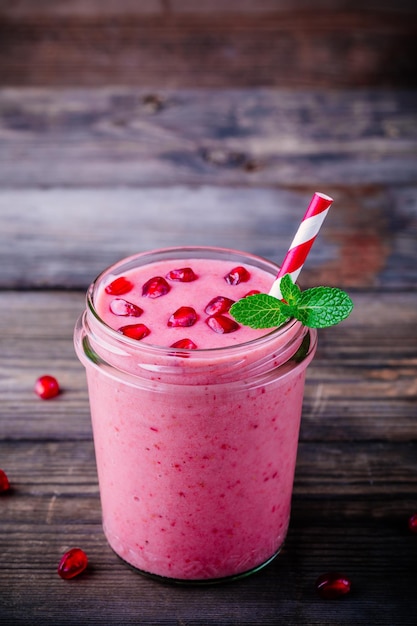 Rosa Granatapfel-Smoothie in einem Glasgefäß mit Minze und frischen Samen auf einem hölzernen rustikalen Hintergrund