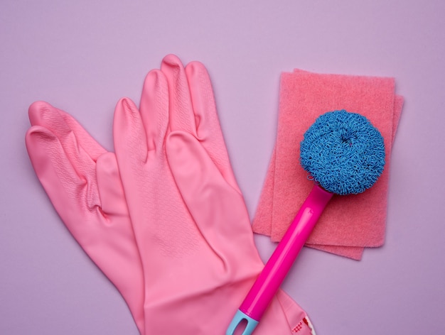 Rosa Gummihandschuhe zum Reinigen, Bürsten auf einem lila Hintergrund, flache Lage