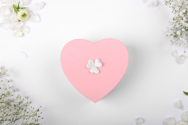Rosa Herzform-Geschenkbox auf einem weißen Hintergrund mit kleinen Withe-Blumen, Feier Valentinstag