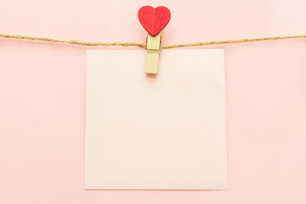 Rosa hoja de papel en blanco en un tendedero y pinzas con corazón rojo sobre un rosa