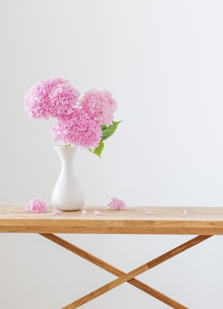 Rosa Hortensie in weißer Vase auf Holzregal auf weißer Hintergrundwand