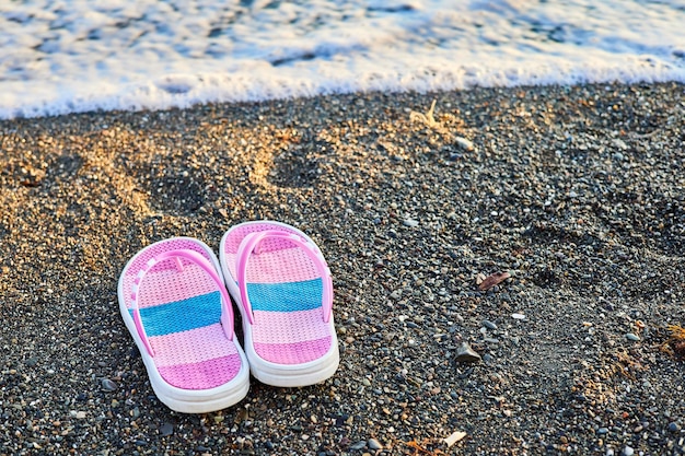 Rosa Kinderpantoffeln an einem Kiesstrand