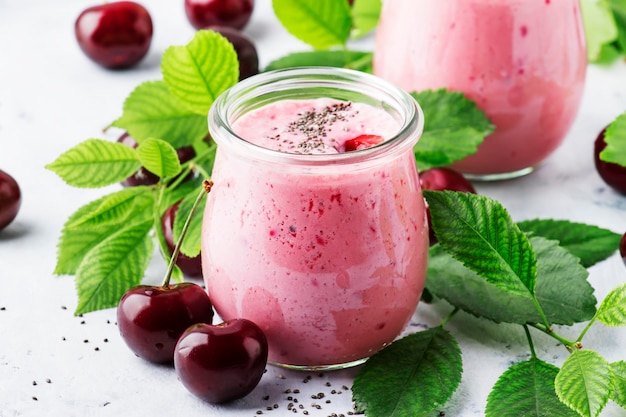 Rosa Kirschsmoothies mit frischer roter Beere und Chiasamen grünen Blättern weißer Steinküchenhintergrundplatz für selektiven Fokus des Textes