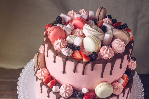Rosa Kuchen rustikal mit Beeren, Marshmallows und Makronen an der Spitze.