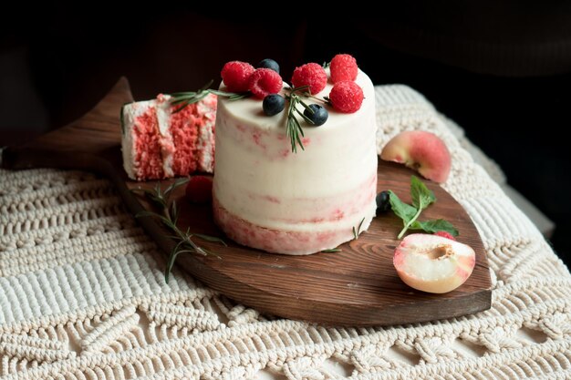 Rosa Kuchen verziert mit Beeren und Früchten auf Holzbrett und Boho-Tischdecke