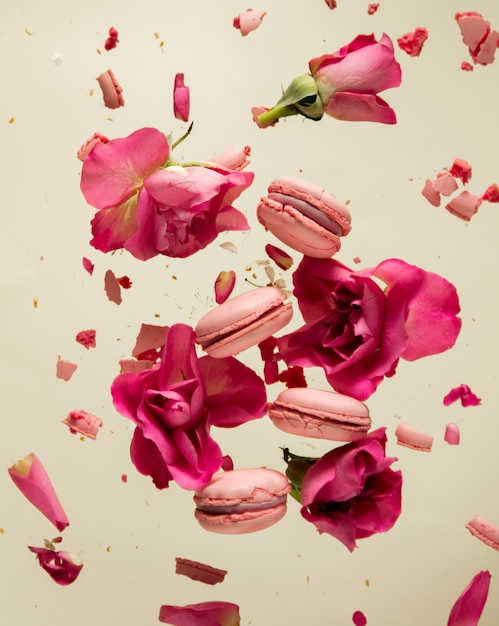 Rosa Makronen und Rosenblätter fliegen in der Luft auf grauer Oberfläche