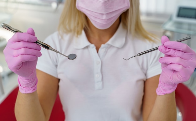 Foto rosa medizinische kittelmaske auf dem gesicht einer ärztin. werkzeuge zur untersuchung der mundhöhle in den händen.