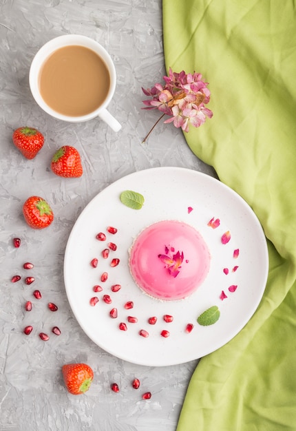 Rosa Moussekuchen mit Erdbeere und einer Tasse Kaffee auf einer grauen Betonoberfläche. Draufsicht.