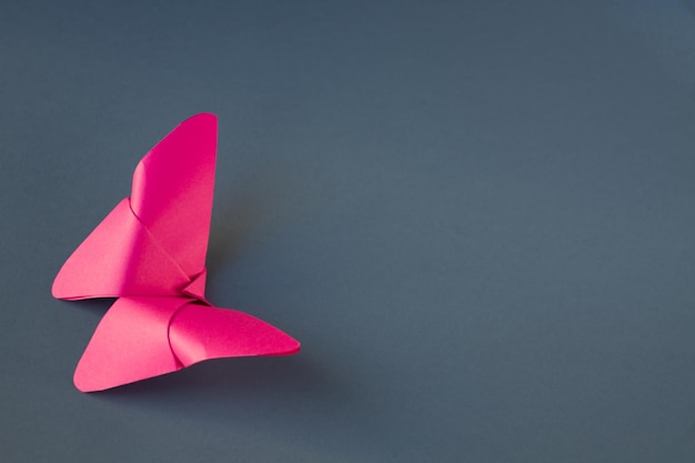 Rosa Papierschmetterlings-Origami lokalisiert auf einem leeren grauen Hintergrund.