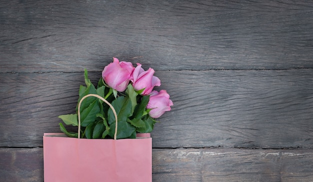 Rosa Papiertüte und rosa Rosen auf hölzernem Hintergrund