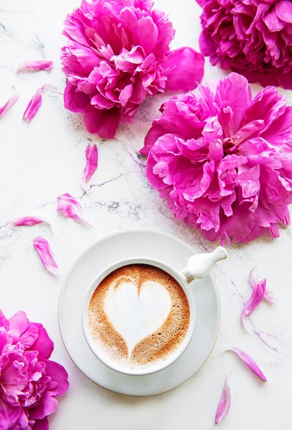 Rosa Pfingstrose und Tasse Kaffee im schönen Stil auf weißem Marmortisch.