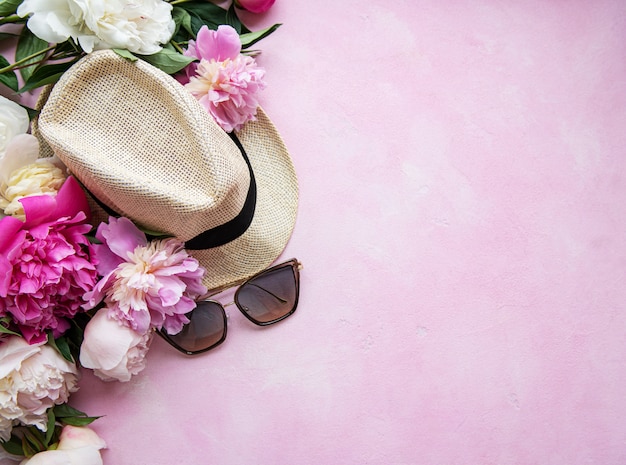 Rosa pfingstrosen und hut auf einem rosa konkreten hintergrund