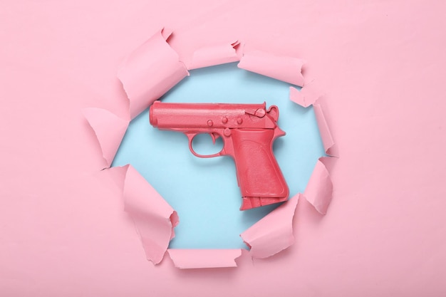Rosa Pistolenpistole auf einem blaurosa zerrissenen Hintergrund Kreatives Konzept Minimalismus Flaches Lay Minimales LayoutDraufsicht