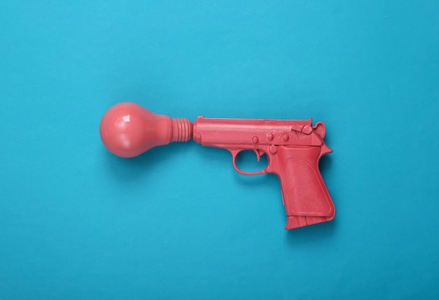 Rosa Pistolenpistole mit Glühbirne auf blauem Hintergrund Kreatives Minimalismus-Layout Frische Idee Konzeptkunst Flache Ansicht von oben