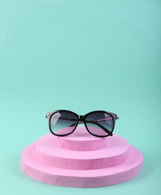 Rosa Podium mit modischer Sonnenbrille auf blauem Hintergrund Produktpräsentation Abstrakte Komposition in minimalistischem Design