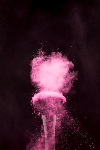 Rosa Pulverexplosion und Make-upbürste auf dunklem Hintergrund