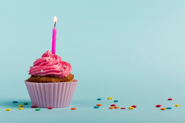 Rosa queimando velas em muffins decorativos com estrela colorida granulado contra o pano de fundo azul