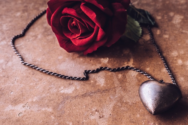 Rosa roja con collar de corazón de plata sobre fondo de tablero de grunge marrón.