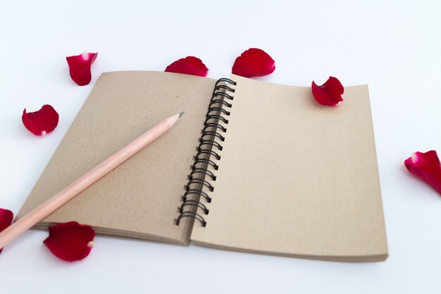 Rosa roja con pétalos y cuaderno marrón.