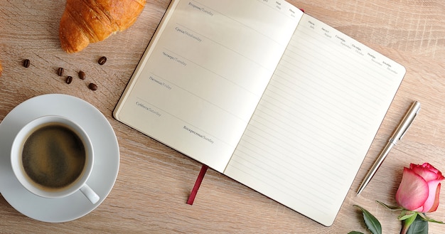 Rosa roja y una taza de café con un croissant y un diario con los días de la semana.