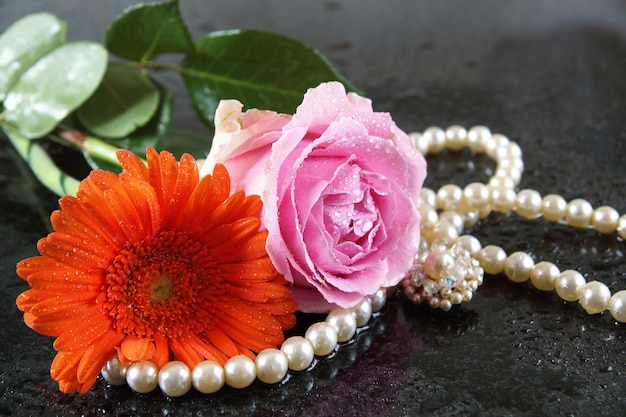 Una rosa rosa y una gerbera naranjal yacen sobre una superficie de granito oscuro