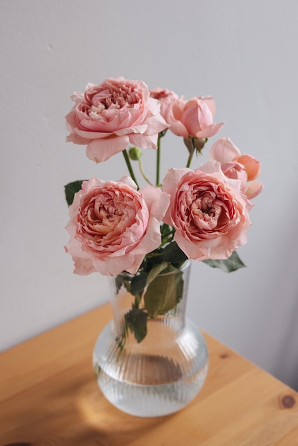 Rosa Rose in der Vase auf Holztisch auf grauer Wand vertikal