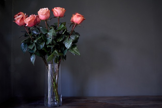 Rosa rosen blühen blumenstrauß in einem klaren hohen kristallvase gegen eine graue wand, selektiver fokus