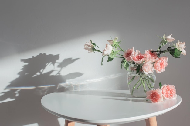 Rosa Rosen im Glasgefäß auf weißem modernen Tisch auf weißer Wand des Hintergrundes
