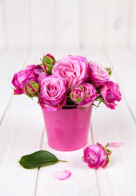 Rosa Rosen im rosa Eimer auf weißem Holztisch