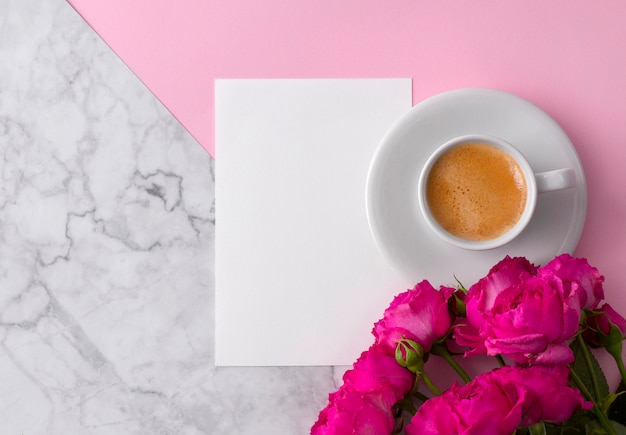 Rosa Rosen mit leerer Grußkarte und Kaffeetasse über rosa Marmor
