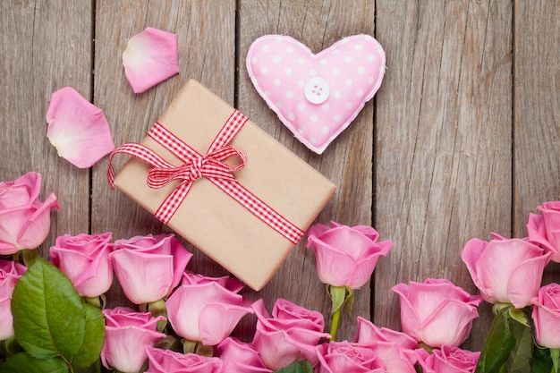 Foto rosa rosen über holztisch mit valentinstag-geschenkbox und herzspielzeug