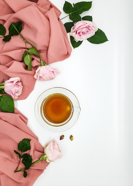 Rosa Rosen und eine Tasse Tee auf weißem Hintergrund