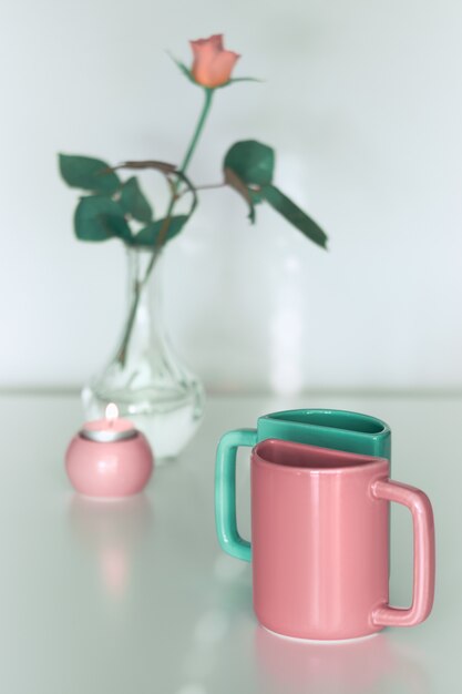 Rosa Rosenblume und zwei halbe Teebecher in lachsrosa und frischem Minzgrün. Minimalistisches Design für Ihr Haus in Pastellfarben. Moderne Inneneinrichtung, romantische Geschenke. Grußkarte zum Valentinstag.