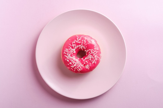 Rosa roter Donut mit weißen Streuseln auf rosa Platte