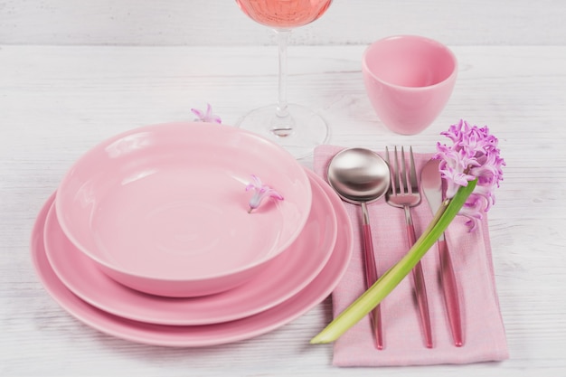 Rosa rustikales Gedeck mit lila Hyazinthenblume und Leinenserviette und Glas Roséwein auf weißer Holzoberfläche
